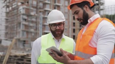 İnşaatçı ve mimar adam inşaat alanı yakınında modern iş merkezi ayakta inşaat planını tartışıyorlar. İşleri bir tabletle kontrol ediyorlar.