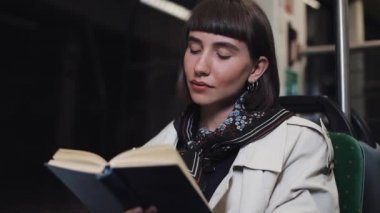 Genç kadın ya da yolcu okuma defteri toplu taşıma da oturan, steadicam vurdu. Yavaş çekim. Şehir ışıkları arka plan. Banliyö, öğrenci, bilgi kavramı.