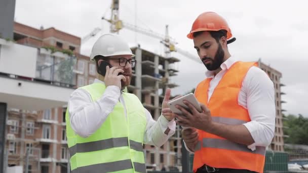 Ingeniero habla en el teléfono móvil en el sitio de construcción y comprueba el trabajo del trabajador. Constructor habla en smartphone. Proyecto inacabado . — Vídeos de Stock