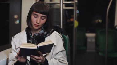 Genç kadın ya da yolcu okuma defteri toplu taşıma da oturan, steadicam vurdu. Yavaş çekim. Şehir ışıkları arka plan. Banliyö, öğrenci, bilgi kavramı.