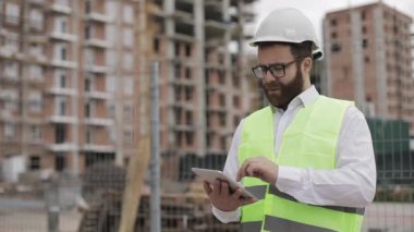 Mimar adam inşaat yerinde tablet ile ayakta ve şeması proje planı analiz. Dışarıda, yavaş hareket.