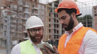 İnşaatçı ve mimar adam inşaat alanı yakınında modern iş merkezi ayakta inşaat planını tartışıyorlar. İşleri bir tabletle kontrol ediyorlar.