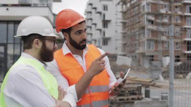 İnşaatçı ve mimar adam inşaat alanı yakınında modern iş merkezi ayakta inşaat planını tartışıyorlar. İşleri bir tabletle kontrol ediyorlar.