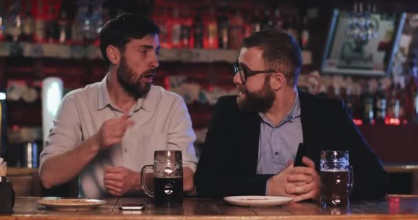 Двоє старих друзів п'ють пиво і розмовляють у спортивному барі. Друзі сидять за барною стійкою, п'ють пиво і розмовляють у пивному пабі . — стокове відео