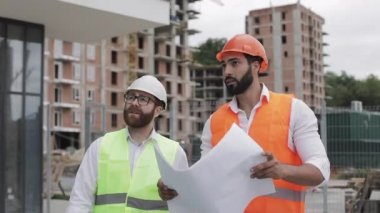 İnşaatçı ve mimar adam inşaat alanı yakınında yürüyen modern iş merkezinin inşaat planı tartışıyorlar. Onlar bir tablet ve mimari taslak ile çalışma kontrol.