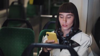Tramvayda çekici genç kadın arkadaşlarıyla sohbet akıllı telefon kullanarak. Yavaş çekim. İnternet, teknoloji, ulaşım, iletişim konsepti.
