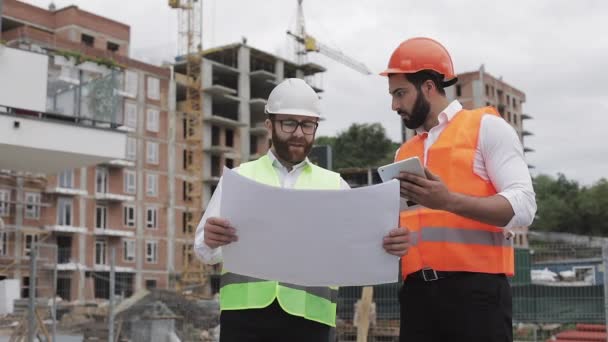 Building a residential complex or business center. Team of engineers men with a tablet and drawing analyzing plans construction builders job activity. — Stock Video
