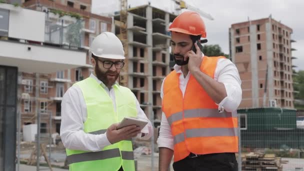 Inżynier mówi na telefon komórkowy na placu budowy i sprawdza pracę pracownika. Budowniczy rozmawia na smartfonie. Niedokończony projekt. — Wideo stockowe