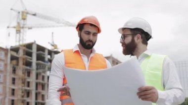Yüksek katlı binanın şantiye veya şantiyemimar ile erkek inşaat mühendisi tartışma. Ellerinde inşaat çizimleri tutuyorlar..