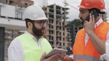 Mühendis inşaat yerinde cep telefonu konuşuyor ve işçi çalışmalarını kontrol eder. Akıllı telefonda Builder görüşmeleri. Bitmemiş proje.