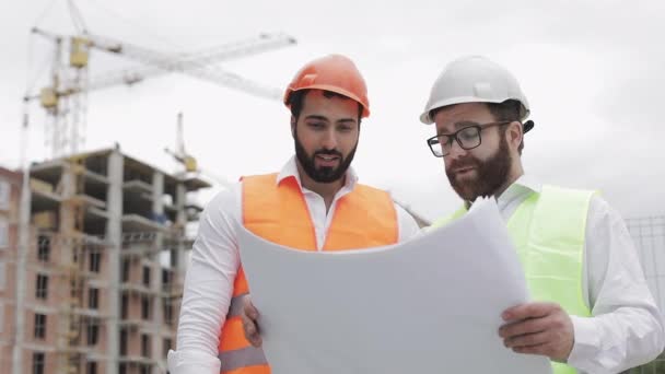 Homme ingénieur construction discussion avec l'architecte sur le chantier de construction ou le chantier de construction de gratte-ciel. Ils tiennent des dessins de construction dans leurs mains . — Video