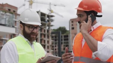 Mühendis inşaat yerinde cep telefonu konuşuyor ve işçi çalışmalarını kontrol eder. Akıllı telefonda Builder görüşmeleri. Bitmemiş proje.