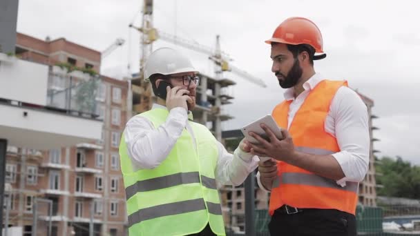 Ingenjör talar på mobil telefon på bygg arbets platsen och kontrollerar arbets tagarens arbete. Builder pratar på smartphone. Oavslutat projekt. — Stockvideo