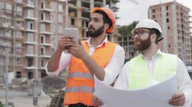 Şantiyede inşaatçı ve mimar tablet işi ile fotoğraf çekmek ve inşaat planı ile kontrol.