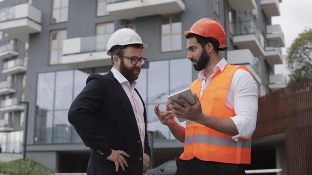 Gerente de construção e arquiteto homem estão discutindo o plano de construção do moderno centro de negócios. Eles verificam o trabalho com um tablet. Fora . — Vídeo de Stock