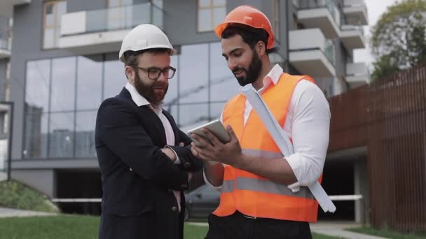 Construction manager and architect man are discussing the construction plan of the modern business center. They checks the work with a tablet. Outside. — Stock Video