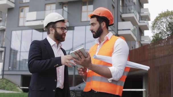 Direttore edile e architetto uomo stanno discutendo il piano di costruzione del moderno centro commerciale. Controllano il lavoro con un tablet. Fuori. . — Video Stock