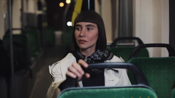 Tired and depressed young woman sitting alone near the transport window. and thinking of something. City lights background. Depressed concept. — Stock Video