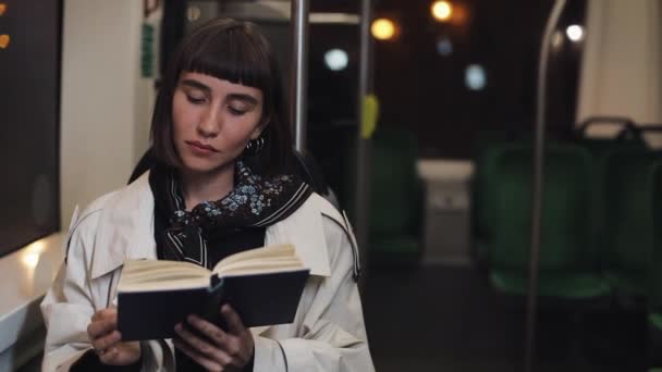 Joven mujer o pasajero leyendo libro sentado en el transporte público, steadicam disparo. En cámara lenta. Fondo de luces de ciudad. Cercanía, estudiante, concepto de conocimiento . — Vídeo de stock