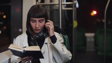 Genç kadın ya da yolcu okuma defteri toplu taşıma da oturan, steadicam vurdu. Yavaş çekim. Şehir ışıkları arka plan. Banliyö, öğrenci, bilgi kavramı.