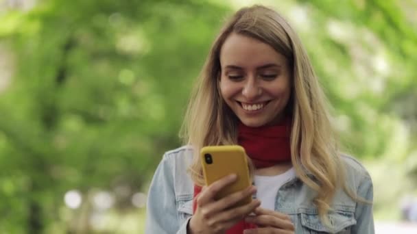 스마트 폰을 사용하여 매력적인 젊은 여성이 공원을 걷고 있습니다. 봄 또는 여름 시간. — 비디오