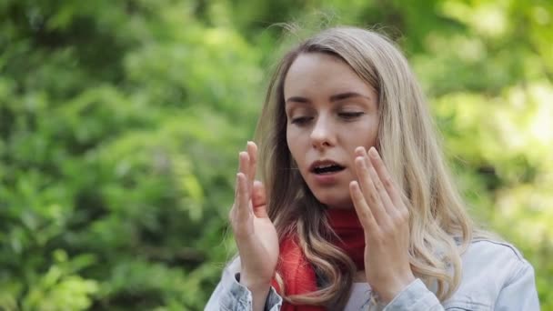 Young woman sneezes and rubs her nose standing on the park background. Allergic rhinitis person. Allergy concept. — Stock Video