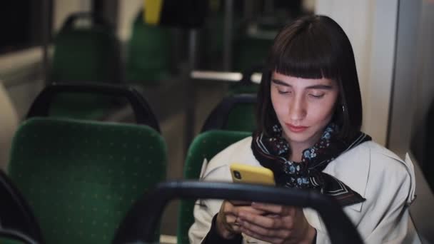 Retrato de jovem mulher elegante navegando no telefone celular em transportes públicos. Jovem mulher de negócios bem sucedida profissional urbana recebendo boas novas. Cidade luzes fundo — Vídeo de Stock