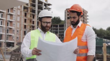 İnşaatçı ve mimar adam, şantiyenin yakınında duran modern iş merkezinin inşaat planını tartışıyorlar. Binaya gidiyorlar..