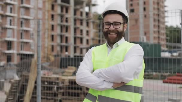 Portrait of smiling architect man standing on the construction site with crossed hands looking at the camera. Outside, slow motion. — Stock Video