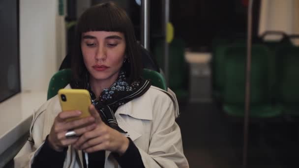 Giovane donna hipster utilizzando smartphone seduto nei trasporti pubblici, colpo costante. Giovane donna riceve buone notizie su smartphone. Al rallentatore. Luci della città sfondo . — Video Stock