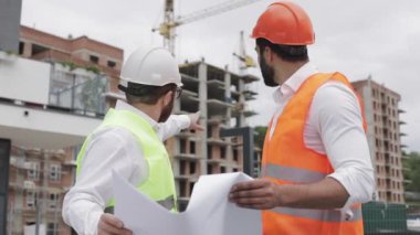 Yüksek katlı binanın şantiye veya şantiyemimar ile erkek inşaat mühendisi tartışma. Ellerinde inşaat çizimleri tutuyorlar..