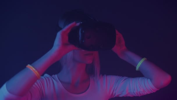 Hermosa joven mirando a su alrededor en gafas de realidad virtual. Iluminación de neón cibernético, fondo abstracto. De cerca. . — Vídeos de Stock