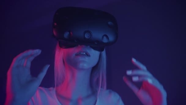 Portrett av en ung, vakker kvinne som fjerner virtuelle virkelighetshodetelefoner på bakgrunn av cyberbelysning . – stockvideo