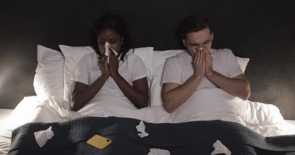 Sick multi-ethnic couple blowing nose lying in the bed. Feeling unwell concept. — Stock Video