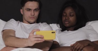 Gece yatakta yatan sarı Smartphone birlikte video izlerken çok etnik çift.