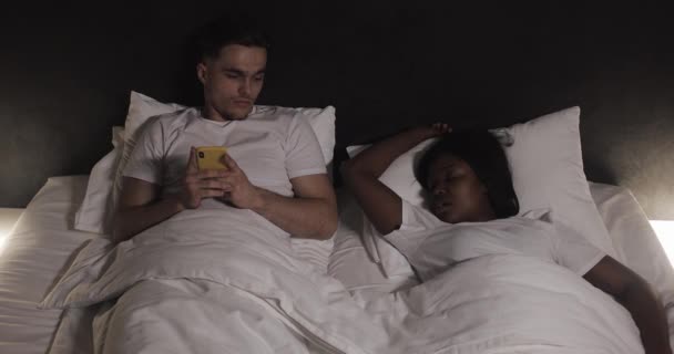 Coppia multietnica sdraiata a letto insieme. L'uomo soffre del fatto che il suo partner russa a letto. Stile di vita di coppia e persone concetto di assistenza sanitaria . — Video Stock