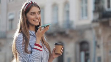 Eski Şehir sokakta bir akıllı telefon ses tanıma fonksiyonu online ayakta kullanarak güzel genç kadın, mobil asistan konuşuyor.