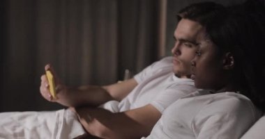 Gece yatakta yatan sarı Smartphone birlikte video izlerken çok etnik çift.