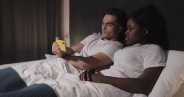 Gece yatakta yatan sarı Smartphone birlikte video izlerken çok etnik çift.