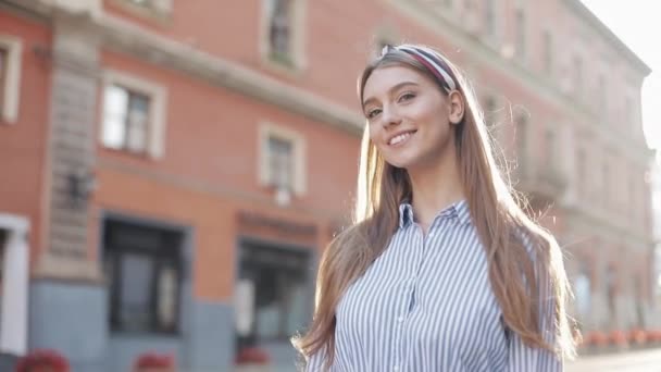 Femme mignonne portant en bleu et blanc robe à rayures chemise marche sur la rue regarder la caméra tourner sourire heureux beau portrait mode visage femelle . — Video