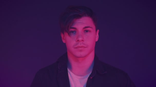 Portrait of handsome young Caucasian male dressed in black shirt looking at camera standing on the neon lights background. People and lifestyle concept. — Stock Video
