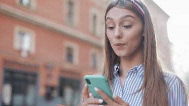 Eski Şehir sokakta Smartphone ayakta uygulama kullanarak mavi ve beyaz çizgili elbise giyen sevimli kadın. Akıllı telefonda iyi haber sahip güzel kız.