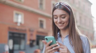 Eski Şehir sokakta Smartphone ayakta uygulama kullanarak mavi ve beyaz çizgili elbise giyen sevimli kadın. Akıllı telefonda iyi haber sahip güzel kız.