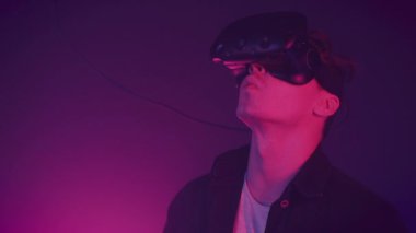 Neon ışıklar arka planda gamepad ile modern sanal gerçeklik kulaklık kullanarak genç çekici adam. Uzaktan kumandalar, tıklama, VR 'de adam çalışması, eller tarafından gesticulating.