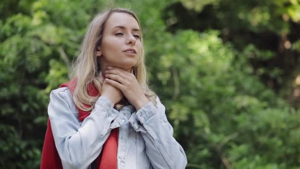 Zieke jonge vrouw dragen rode sjaal gevoel slecht lijden aan keelpijn, staande in het Park. Pijnlijk slikken, hoesten, gezondheid concept. — Stockvideo