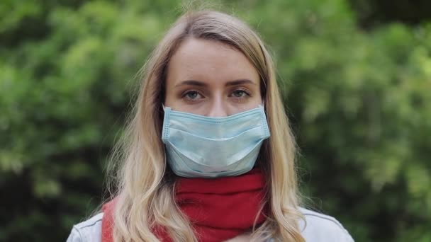 Giovane donna in una maschera sterile purtroppo guardando nella fotocamera in piedi nel parco sullo sfondo dell'albero. Autunno o primavera allergia . — Video Stock