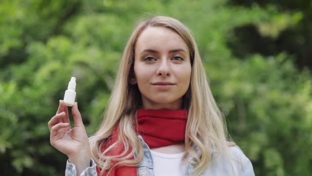 Retrato de una hermosa mujer sonriente con bufanda roja sosteniendo aerosol nasal alérgico en su mano de pie en el parque de la ciudad. Concepto de Salud. Medicina . — Vídeos de Stock