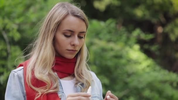 Giovane donna che indossa sciarpa rossa spruzzando spray nasale in piedi nel parco cittadino. Concetto di terapia sanitaria Concetto. Medicina. — Video Stock