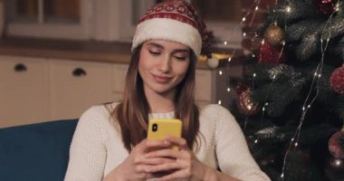 Güzel Genç Sarışın Kafkas Lady Noel Ağacı yakınında Oturan Santas Şapka Giyen Tatil ve Yeni Yıl Close Up onu Smartphone Kavramı kullanarak.