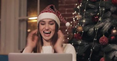 Noel Şapkası Giyen Genç Güzel Kadınlar Evde Arka Planda Kanepede Oturan Onu Laptop Kullanarak Smiles ve Tatil ve Yeni Yıl Kavramı Gülüyor.